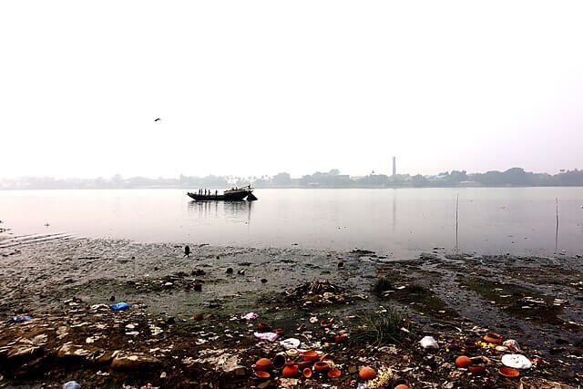 Plastic waste and discarded rubbish scattered along the bank of a river, highlighting the impact of river pollution on ecosystems.