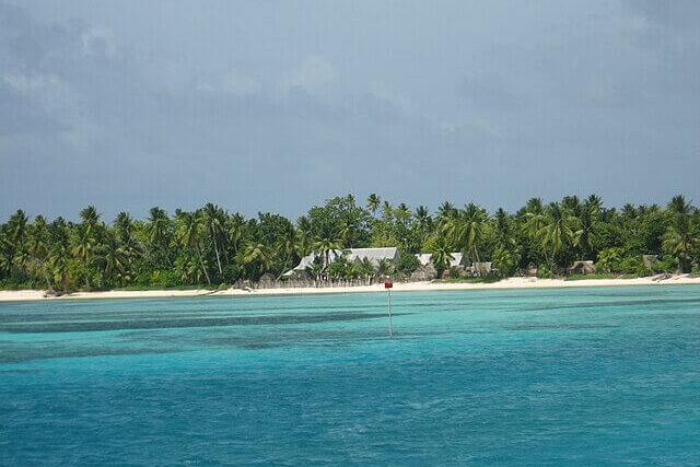 Low-lying atoll islands in Kiribati with palm trees and homes close to the shoreline, highlighting the country’s vulnerability to coastal flooding and rising sea levels.