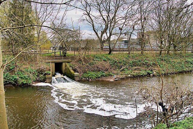 River Irwell flowing past a sewage treatment works with visible industrial infrastructure along the riverbank
