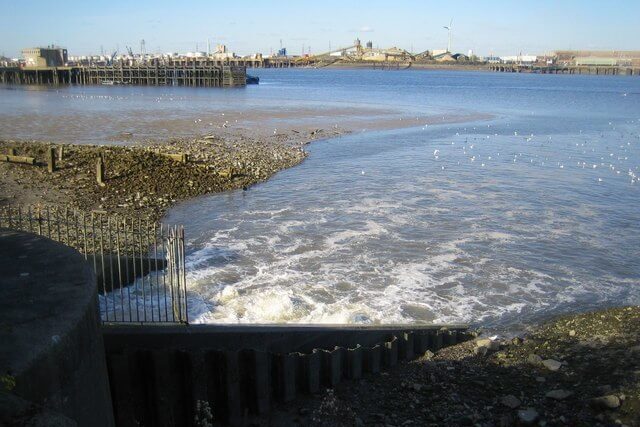 Sewage overflow outlet at Crossness on the River Thames discharging into the water near industrial structures