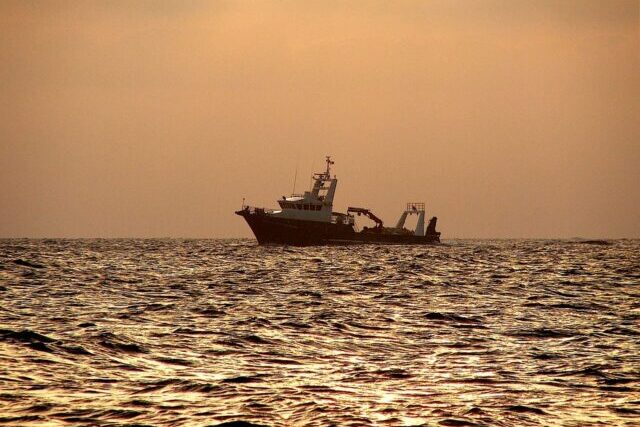 Large commercial fishing trawler operating in the Pacific Ocean with nets and equipment on deck under open blue skies.
