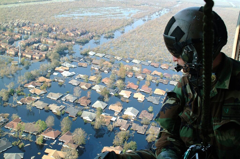 Aerial view from a military helicopter showing extensive flooding across New Orleans after Hurricane Katrina, with water covering residential neighbourhoods and infrastructure.