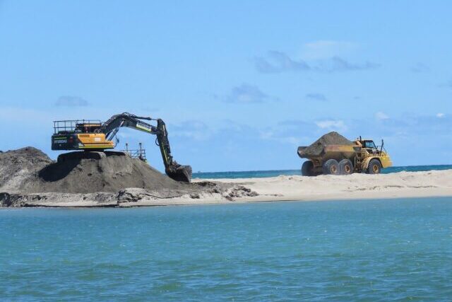 Heavy machinery including an excavator and dump truck operating at a sand mining site, extracting and transporting sand for construction use.