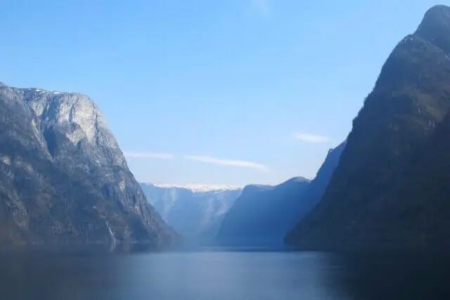 Panoramic view of Sognefjord in Norway surrounded by steep mountains, deep blue water and small coastal settlements under cloudy skies.
